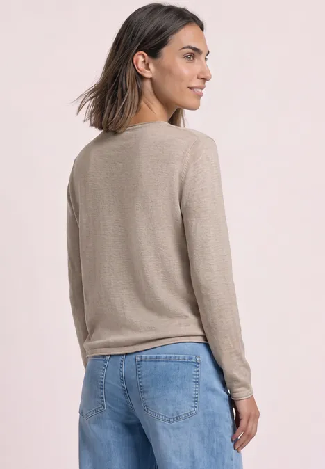 Frau von hinten in beigem Pullover und blauer Jeans, schaut seitlich.