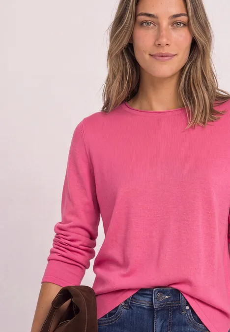 Frau in pinkem Pullover und Jeans vor weißem Hintergrund