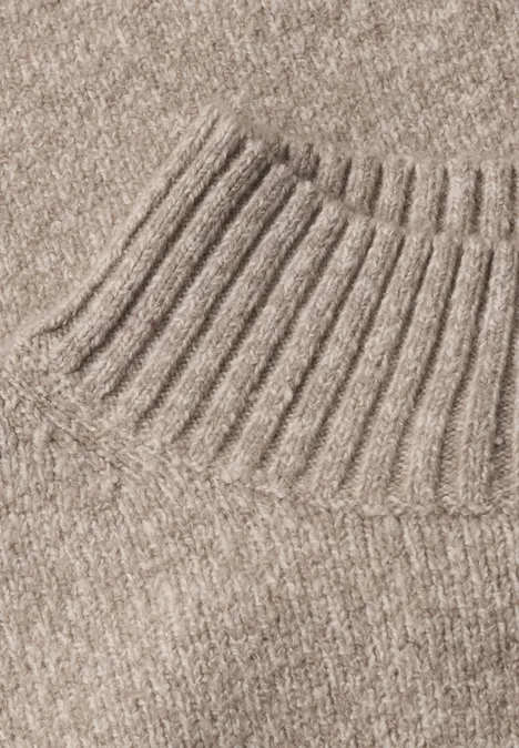 Gros plan sur un pull en maille beige avec col roulé côtelé.