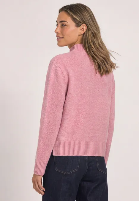 Frau in rosa Pullover und blauer Jeans, leicht seitlich stehend.