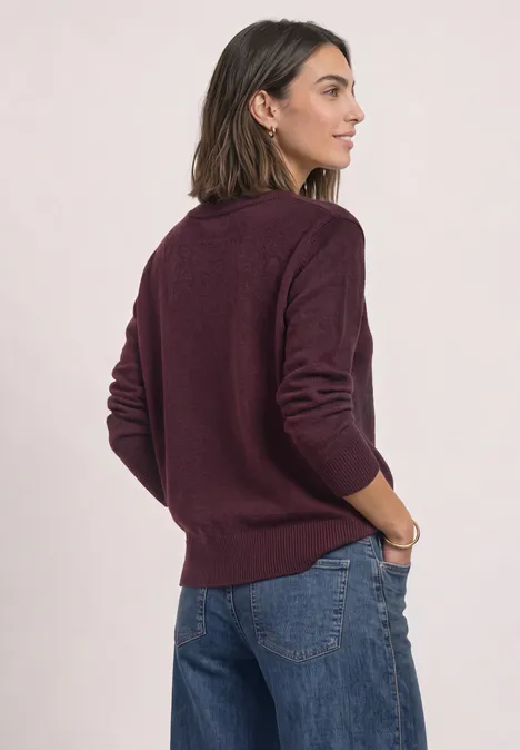 Femme vue de dos portant un pull bordeaux et un jean, main gauche dans la poche.