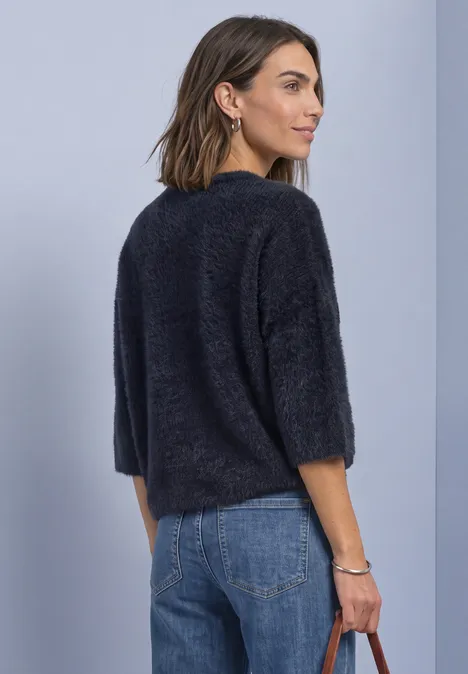 Vrouw in zijaanzicht met zwart, zacht trui met 3/4-mouwen en blauwe jeans.