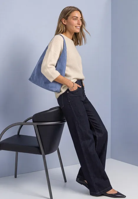 3/4-Arm Pullover mit Rundhals pure beige Frau mit weitem Jeans, hellblau-beige Oberteil und blauer Tasche lehnt an Stuhl vor minimalistischem Hintergrund.
