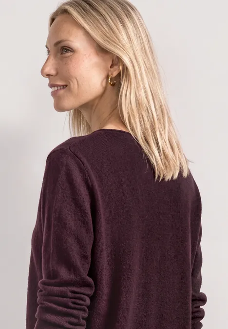 Eine Frau mit blondem Haar trägt einen weinroten Pullover und blickt zur Seite.