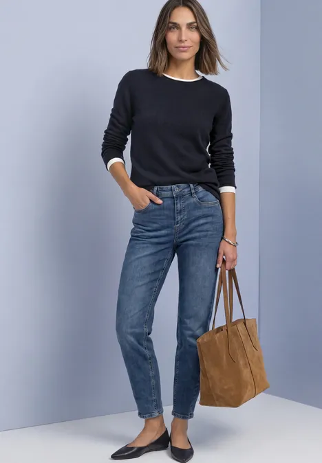 Pullover mit Boat Neck und Rollkanten indigo night Frau in schwarzem Pullover, blauen Jeans und schwarzen Loafers, hält eine braune Tasche.