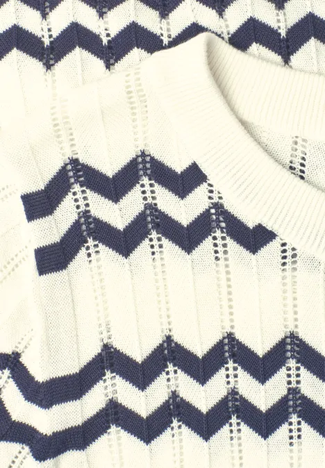 Nahaufnahme eines weißen Strickpullovers mit dunkelblauen Zickzack-Streifen.