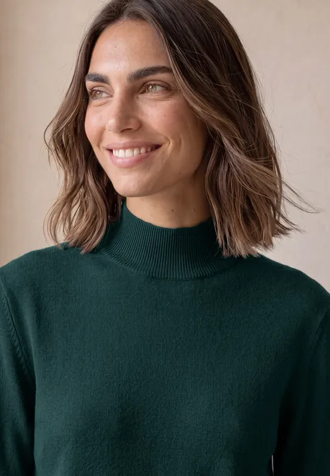 Basic sweter z golfem shadow teal Uśmiechnięta kobieta o średniej długości kasztanowych włosach, ubrana w zielony golf na jasnym tle.