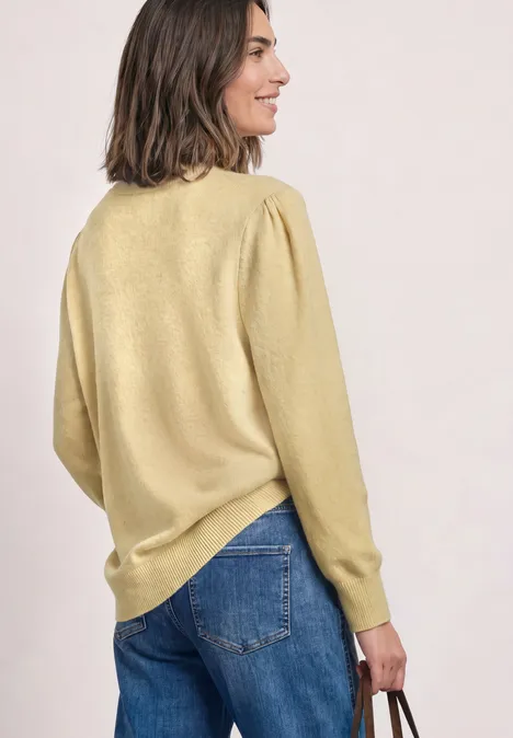 Pull à manches longues, col rond et fronces sunbeam yellow mel. Femme de dos en pull jaune et jean, vue de côté, tenant un sac à la main droite.