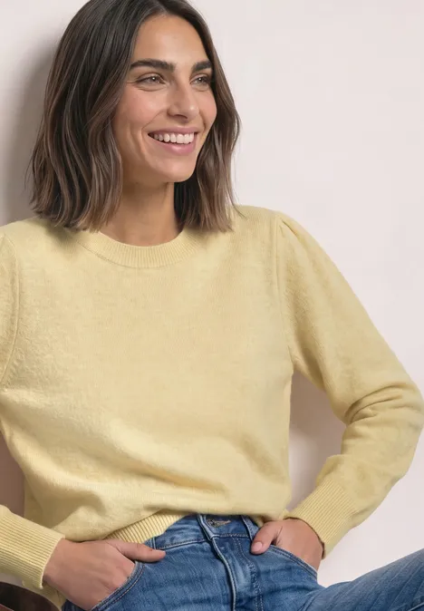 Pull à manches longues, col rond et fronces sunbeam yellow mel. Femme souriante en pull jaune pastel et jean bleu, mains dans les poches.