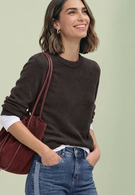 Pull à manches longues, col rond et fronces black coffee mel. Jeune femme souriante en pull marron sur chemise blanche, jean et sac bandoulière rouge.