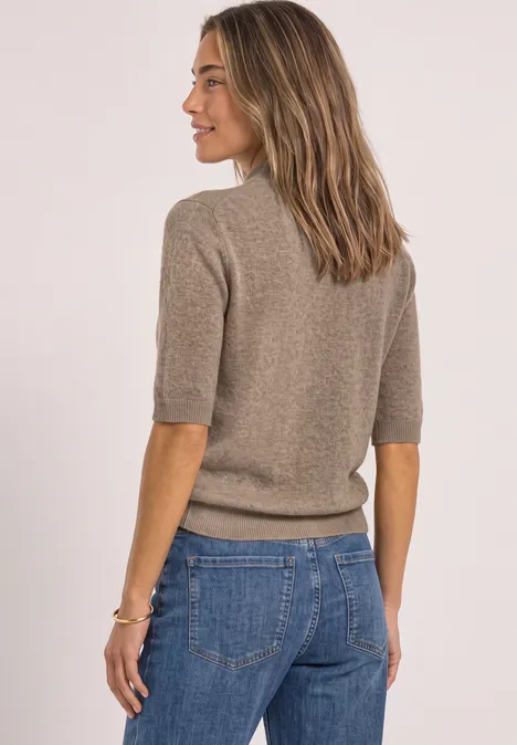 Frau von hinten in taupefarbener Strickjacke mit halblangen Ärmeln und blauen Jeans.