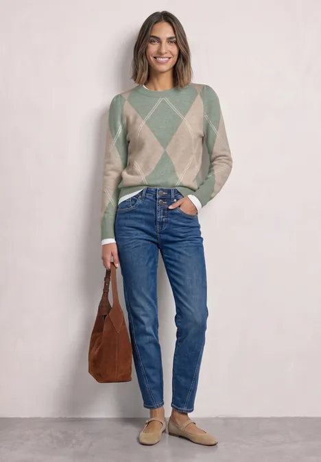Vrouw in grijs-beige ruittrui, blauwe jeans, beige loafers en een bruine tas.