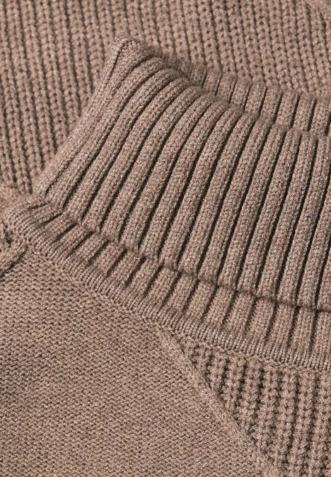 Nahaufnahme eines beigen, gerippten Rollkragen-Pullovers aus weichem Strick.