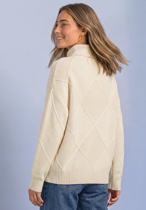 Frau in cremefarbenem Strickpullover mit Rautenmuster, lächelnd seitlich zur Kamera blickend