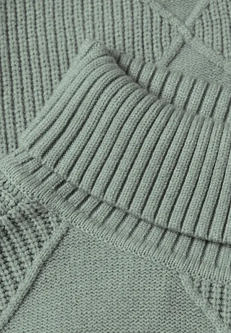 Nahaufnahme eines pastellgrünen Strickpullovers mit Rippenmuster und diagonaler Naht.