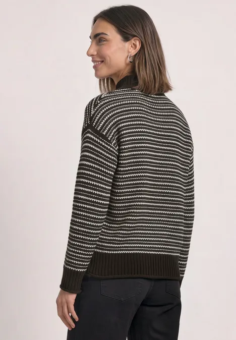 Een vrouw met kort haar draagt een gestreepte trui en kijkt over haar schouder met een lichte glimlach.