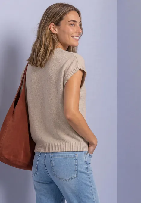 Pull sans manches à col rond light sepia sand Junge Frau in beigem Stricktop, Jeans und brauner Tasche schaut lächelnd über die Schulter.