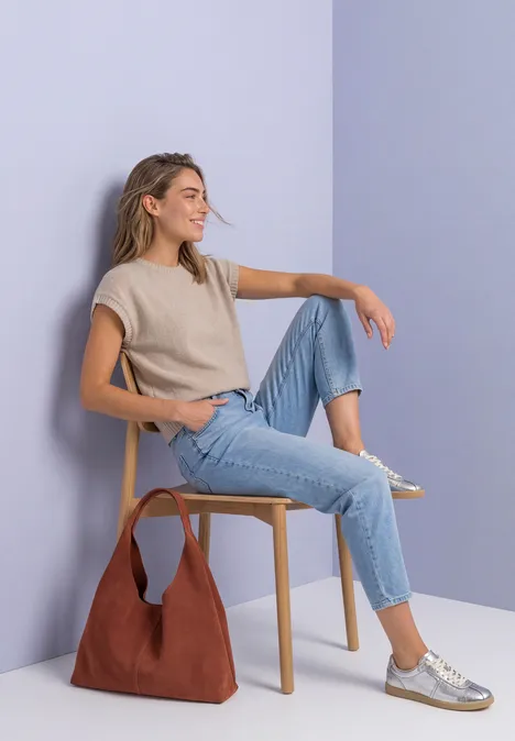 Pull sans manches à col rond light sepia sand Eine Frau sitzt entspannt auf einem Stuhl, trägt Jeans, beiges Top und silberne Sneaker, Tasche am Boden.