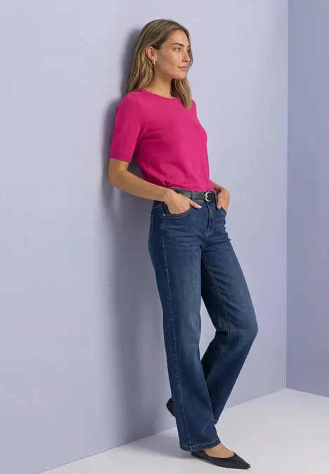 Pull à manches courtes et col rond, de couleur unie magenta dream Eine Frau lehnt an der Wand, trägt pinkes Shirt, blaue Jeans und schwarze Ballerinas.