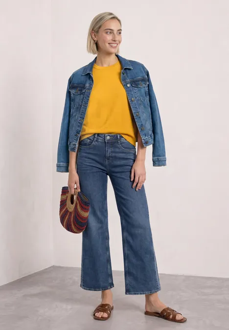 Eine Frau trägt gelben Pullover, weite Jeanshose, Jeansjacke und Handtasche.