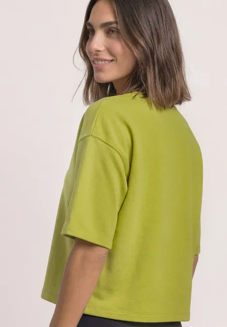 Kurzarm Sweatshirt mit Rundhals apple lime Frau mit halblangen braunen Haaren blickt lächelnd über die Schulter auf ein limettengrünes, kastiges T-Shirt.