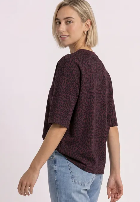 Kurzarm Sweatshirt mit Rundhals rustic rouge Frau in gemustertem, violett-rotem T-Shirt und Jeans, blickt über ihre Schulter.