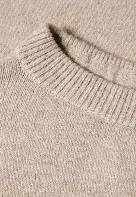 Close-up van een beige gebreide trui met geribbelde ronde hals.