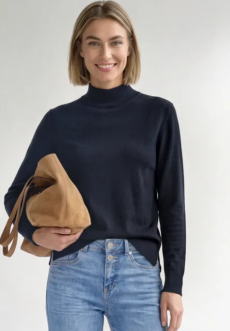 Basic sweter z golfem darkest blue Kobieta z krótkimi jasnobrązowymi włosami w czarnym golfie i niebieskich dżinsach trzyma brązową torbę.