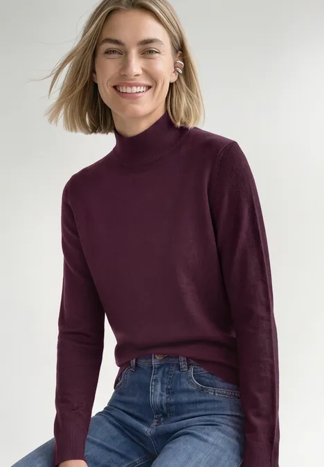 Basic sweter z golfem berry maroon Uśmiechnięta kobieta w bordowym golfie i niebieskich dżinsach.