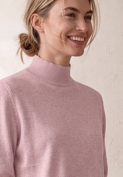 Basic sweter z golfem quiet rose mel. Młoda kobieta z włosami związanymi w kucyk, w różowym golfie, uśmiecha się na jasnym tle.