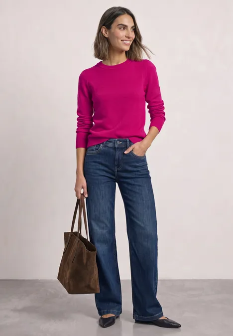 Femme en pull fuchsia et jean large, portant un sac marron.