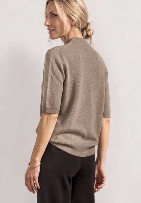 Kurzarm Pullover mit Turtle Neck sanded amber mel. Frau von hinten in beigem Kurzarm-Pullover und schwarzer Hose, mit locker gebundenem Dutt.