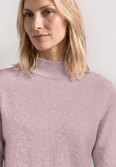 Kurzarm Pullover mit Turtle Neck quiet rose mel. Eine Frau mit blondem Haar trägt einen fliederfarbenen Rollkragenpullover und lächelt dezent.