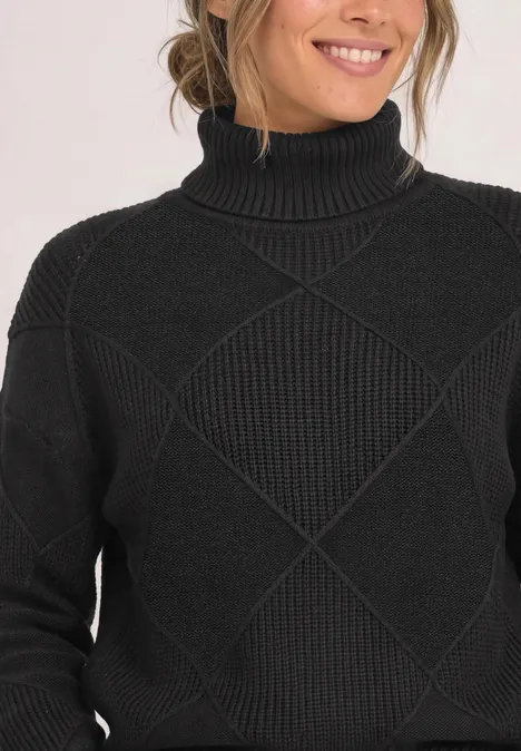 Schwarzer Rollkragenpullover mit Rautenmuster, fotografiert am Oberkörper einer lächelnden Person.
