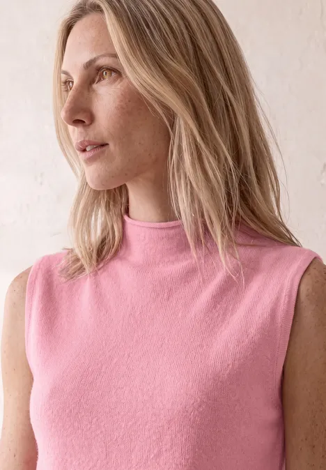 Een blonde vrouw in een mouwloze roze top kijkt zijwaarts naar links.
