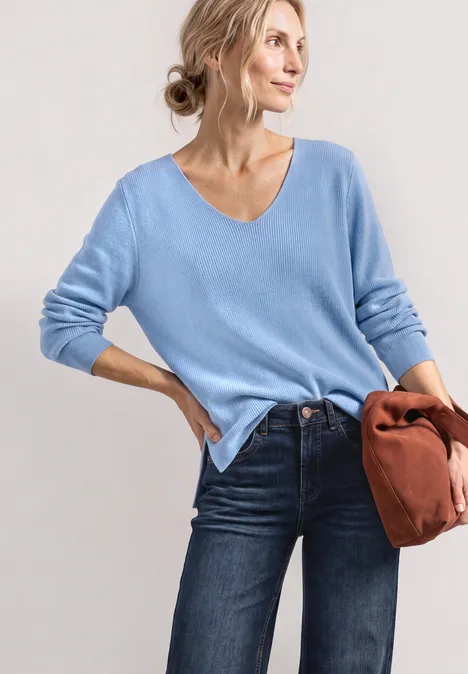 Langarm Pullover mit V-Ausschnitt northern blue Frau trägt hellblauen V-Pullover und Jeans, hält braune Tasche, lässige Pose.
