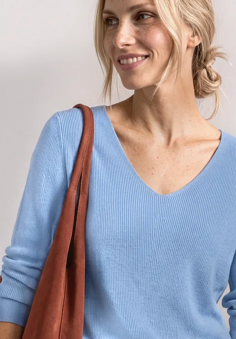 Langarm Pullover mit V-Ausschnitt northern blue Eine blonde Frau in einem hellblauen Pullover mit brauner Tasche über der Schulter.
