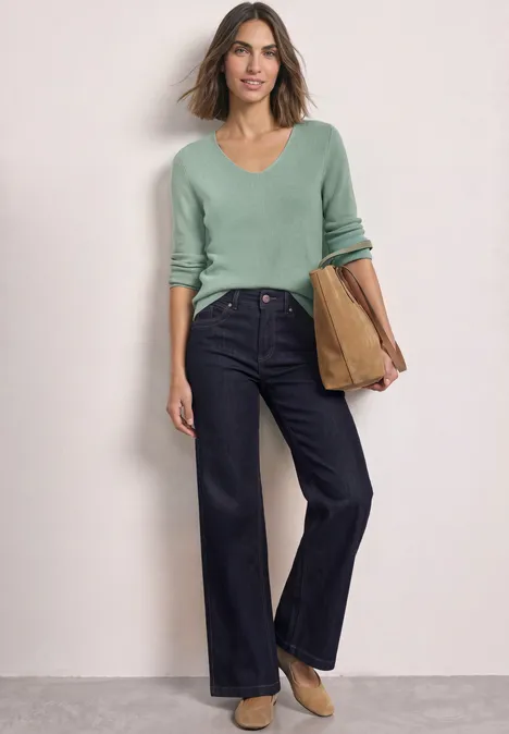 Langarm Pullover mit V-Ausschnitt eucalyptus green Eine Frau in weiter dunkelblauer Jeans und mintgrünem Pullover hält eine Tasche.