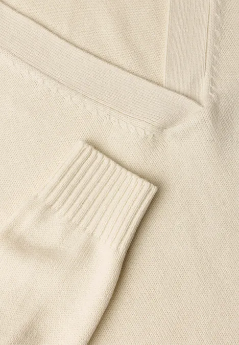 Nahe Aufnahme eines cremefarbenen Strickpullovers mit V-Ausschnitt und Rippbündchen.