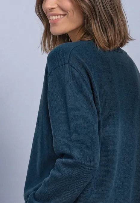 Eine lächelnde Frau mit schulterlangem braunem Haar im dunkelgrünen Pullover vor hellem Hintergrund.