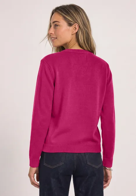 Frau von hinten in pinkem Pullover und dunkler Jeans vor hellem Hintergrund.