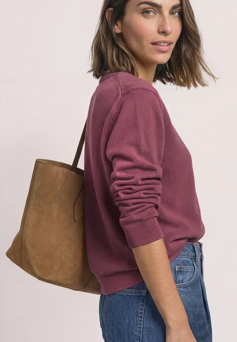 Frau in violettem Pullover und Jeans trägt eine braune Schultertasche, seitliche Ansicht.