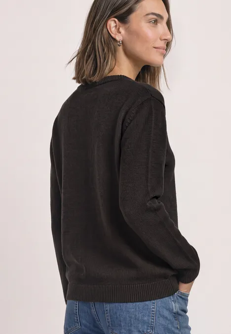 Frau in schwarzem Pullover und Jeans schaut seitlich.