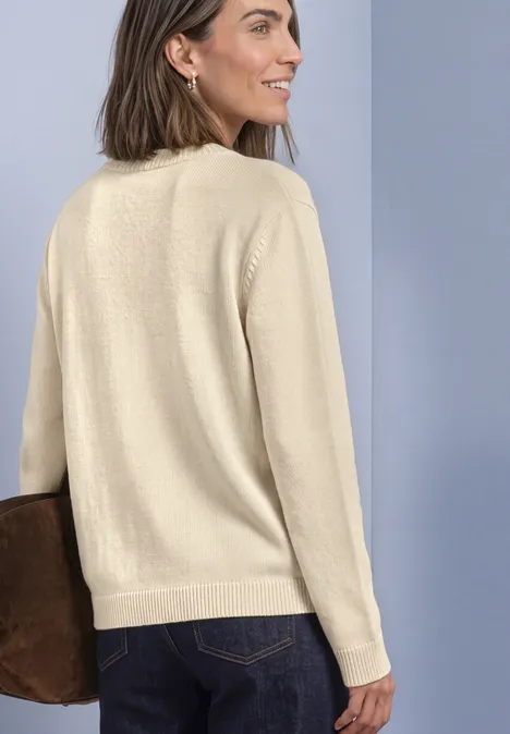 Frau von hinten in hellbeigem Pullover und dunkler Jeans, mit brauner Tasche vor grauem Hintergrund.