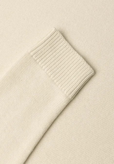 Nahaufnahme eines cremefarbenen Strickpullover-Ärmels mit Rippbündchen