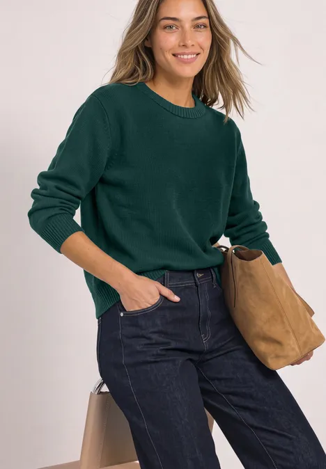 Langarm Pullover mit Boat Neck shadow teal Eine junge Frau in dunkelgrünem Pullover, Jeans und beiger Tasche, die lächelnd in die Kamera schaut.
