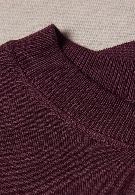 Nahaufnahme eines burgunderroten Strickpullover-Ausschnitts auf beigem Strickuntergrund.
