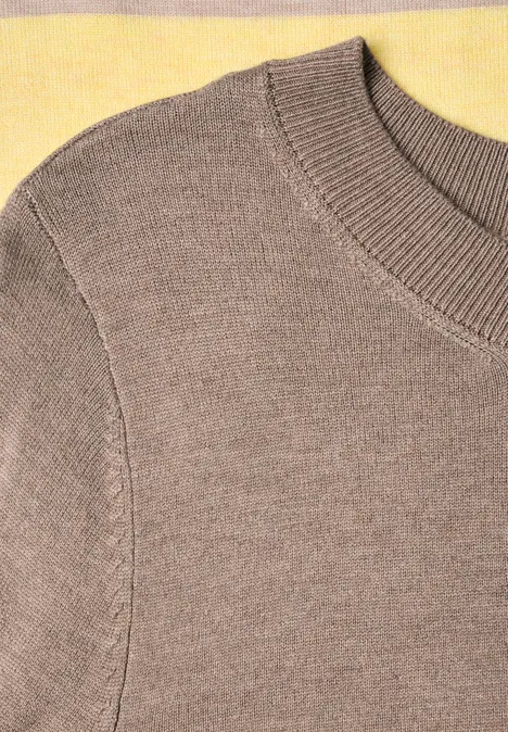 Nahaufnahme eines beigen Strickpullovers mit Rippenmuster am Ausschnitt und Ärmelansatz.