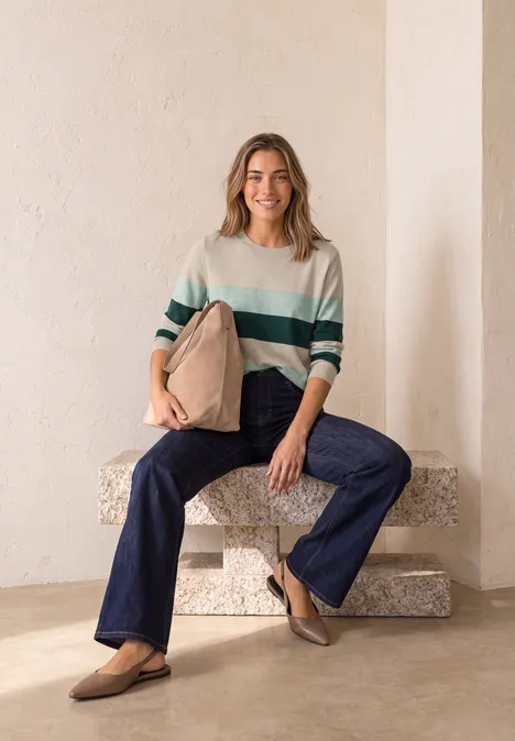 Pullover mit Rundhals und Streifen clay sand mel. Frau sitzt auf einem steinernen Block, trägt gestreiften Pullover, Schlagjeans und Loafers, hält eine beige Tasche.