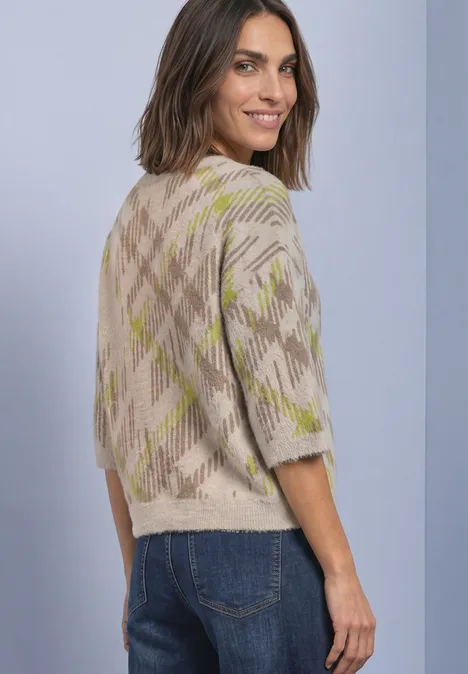 Frau in beigem Strickpullover mit Karomuster, schaut über die Schulter.